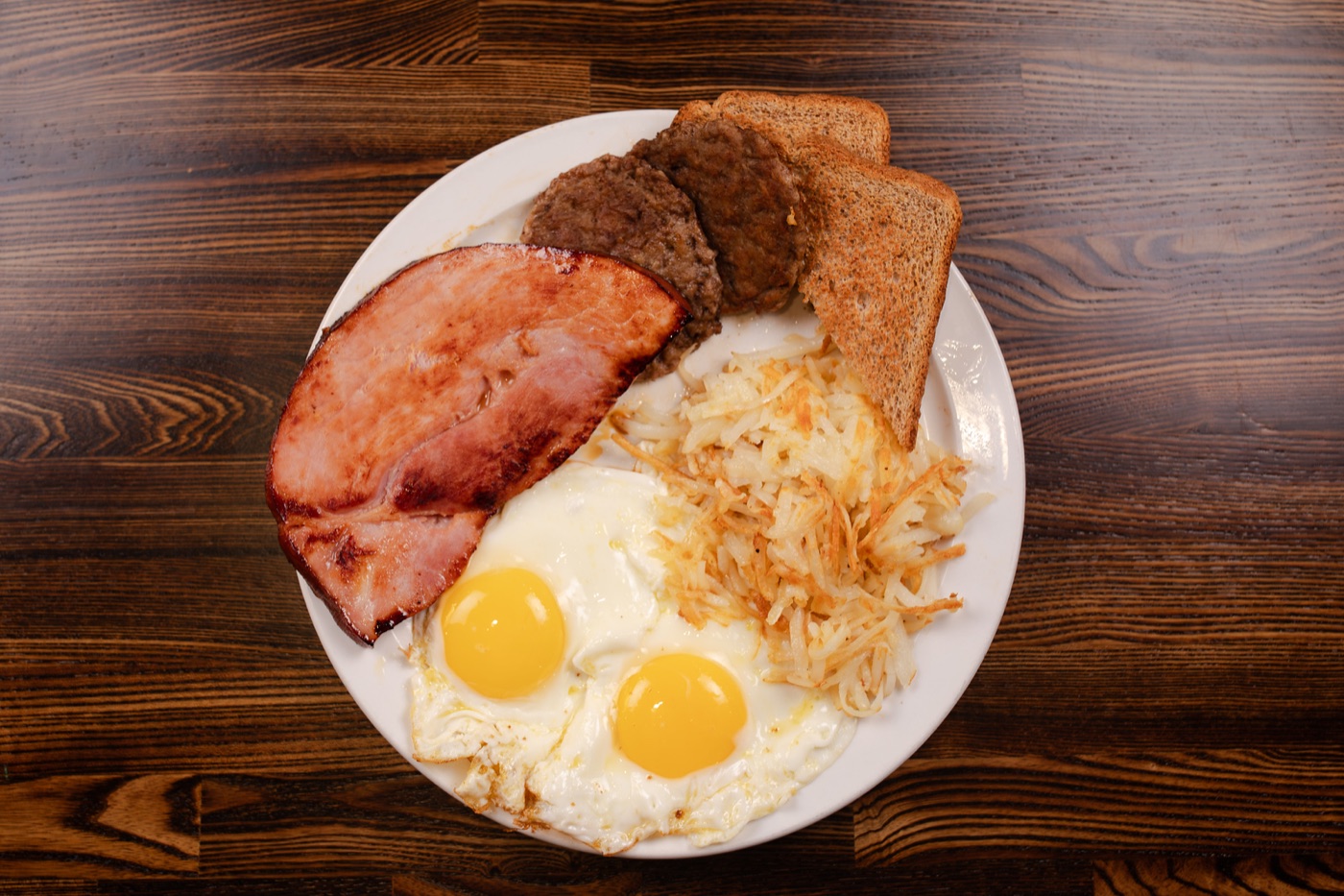 Breakfast plate with eggs, ham, sausage, toast and hash browns