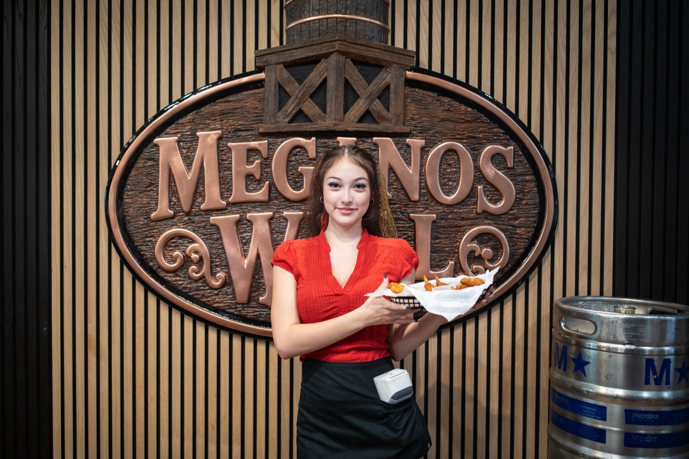 A server holding a plate in front of the carved Meganos Well sign